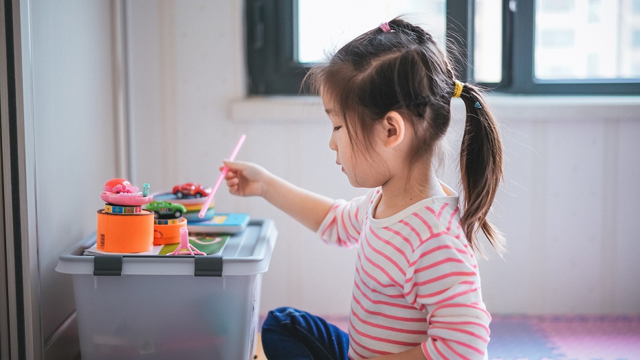 A little girl in a striped shirt plays with construction toys