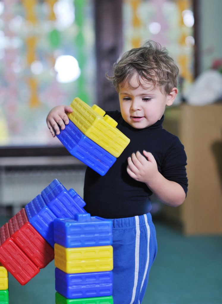 A toddler boy builds a tower with big colorful plastic blocks.