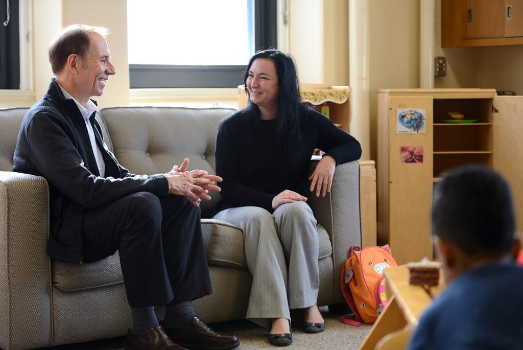 A man and a woman smile as they talk on a couch in a preschool classroom