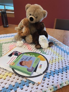 Three teddy bears, a newborn diaper and other materials for the session sit on a crocheted baby blanket