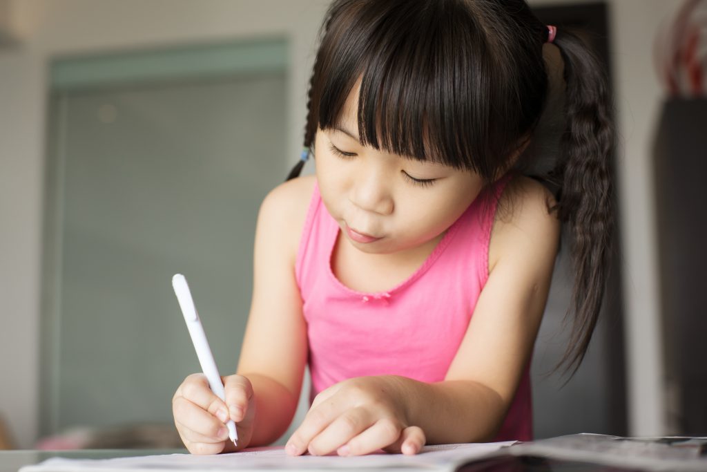 Photo of a little girl practicing writing with a pen and paper