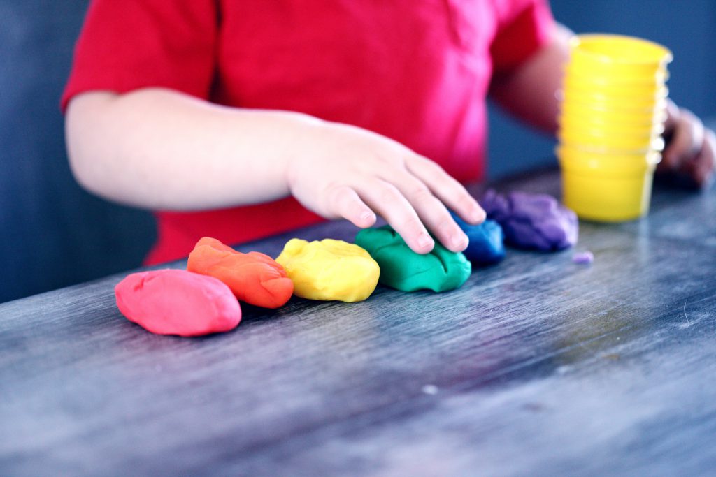 A child plays with a row of multicolored lumps of clay