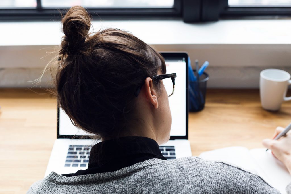 Woman working on laptop and taking notes on notepad