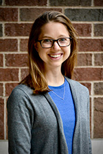 Christiana Raymond-Pope, PhD, in blue shirt with grey sweater smiling in front of brick wall