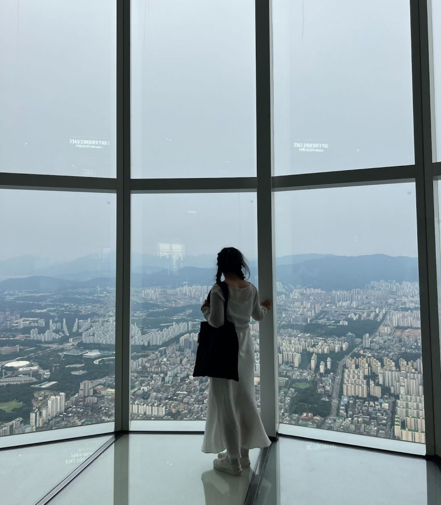 Mai Soua Vang overlooking a city in South Korea via a window in a tall building