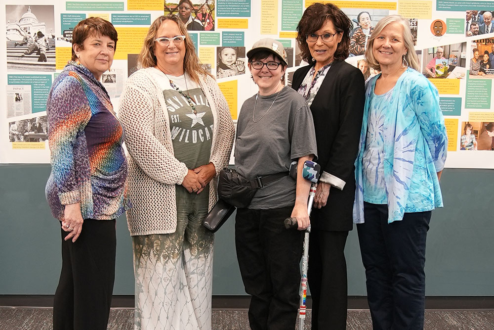 Heidi Myhre (center) stands in front of a timeline of Impact articles and images with current and former ICI staff. On the left are Angela Amado (former ICI staff member) and ICI's current Director, Amy Hewitt. On the right are former ICI staff members Teri Wallace and Beth Fondell.